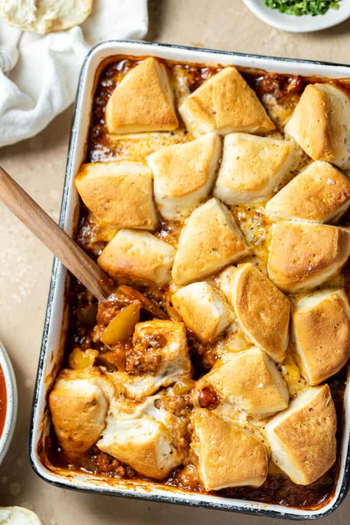 Sloppy joe biscuit bake recipe in a baking dish with a wooden spoon.