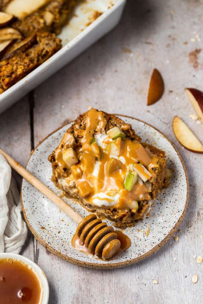 Spiced pear oatmal topped with yogurt and nut butter on a plate with honey.