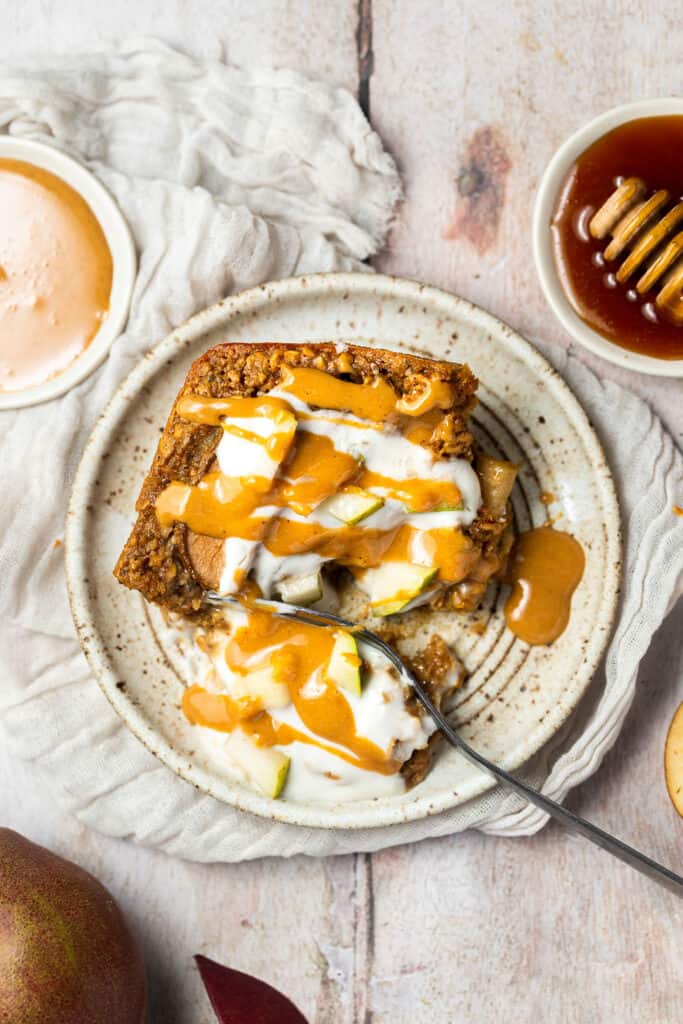Spiced pear oatmal topped with yogurt and nut butter on a plate with a fork.