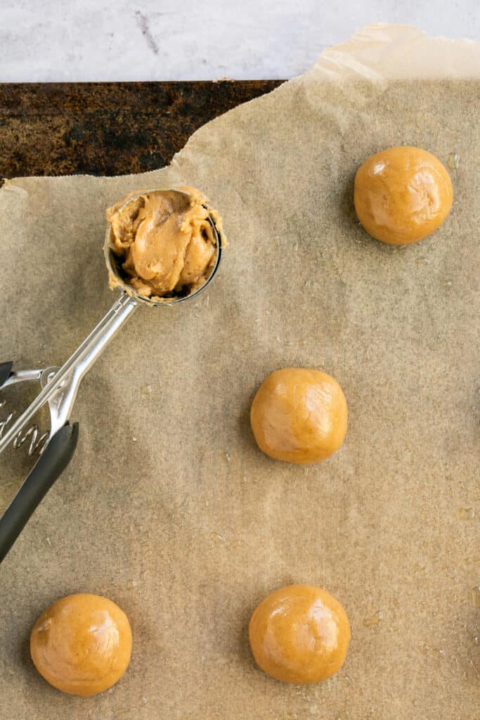 Ball of cookie dough placed on parchment paper with a cookie scoop.