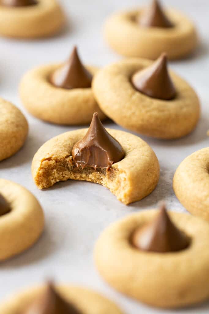 Peanut butter blossom cookies on parchment paper, one with a bite take out of it.