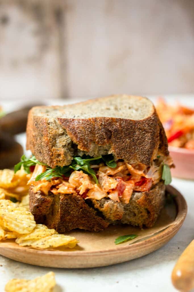 Creamy buffalo chicken salad on two pieces of bread with chips on plate.