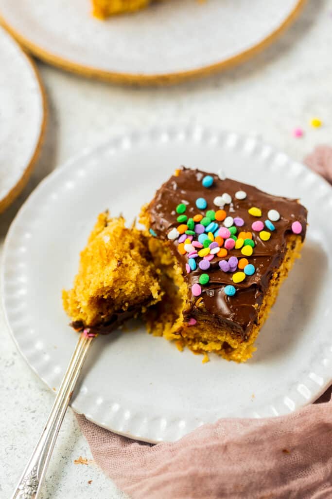 A slice of Healthy yellow cake topped with chocolate frosting and sprinkles on a small plate with a fork.