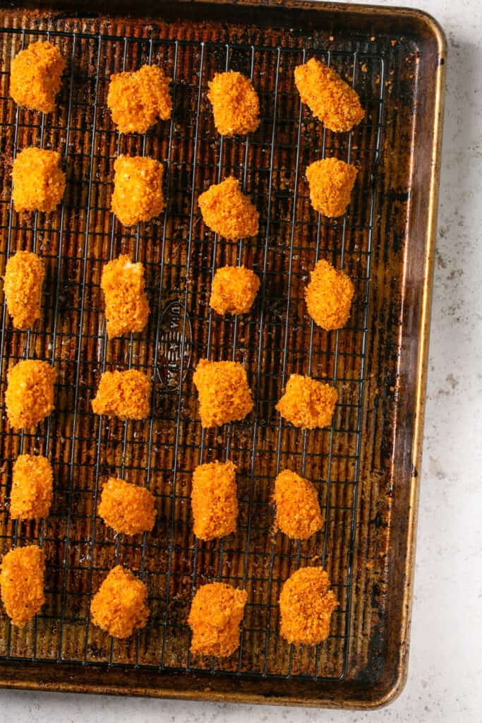 Panko baked chicken nuggets on a cooling rack on a baking sheet.