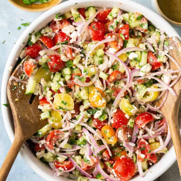 Tomato cucumber salad in a large bowl with a wooden spoon.