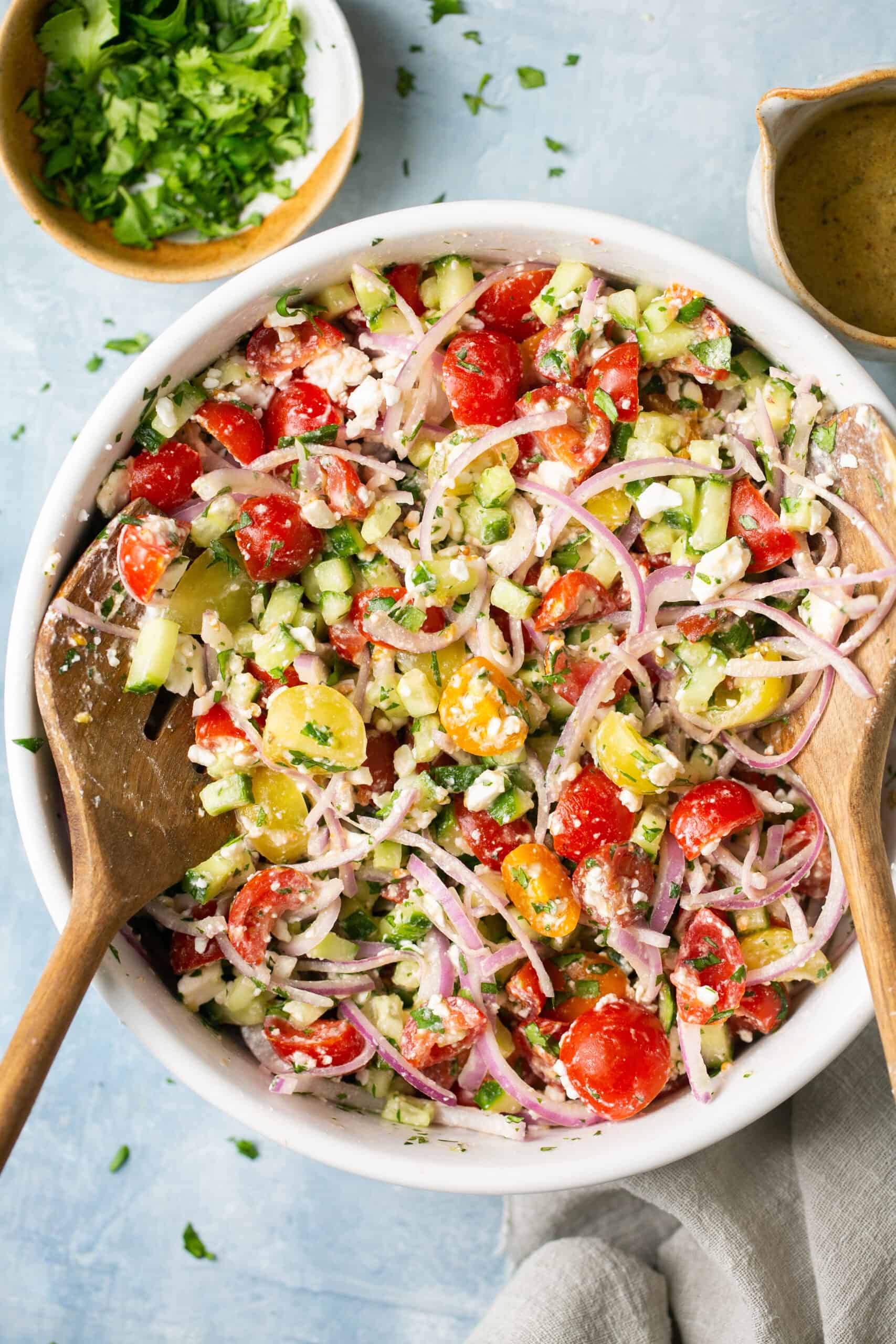 Tomato cucumber salad in a large bowl with a wooden spoon.