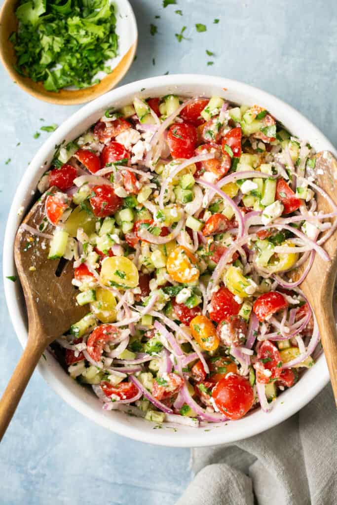 Tomato cucumber salad in a large bowl with wooden tongs.
