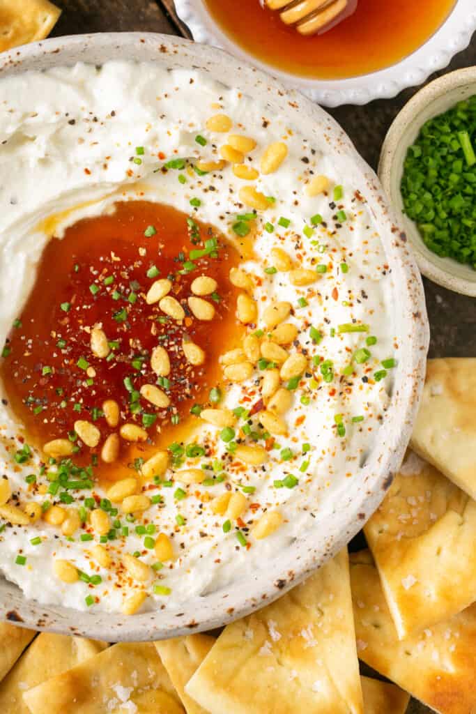 Pita bread being dipped in whipped feta with honey topped with pine nuts and chopped chives.
