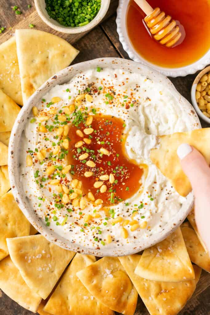 Pita bread being dipped in whipped feta with honey topped with pine nuts and chopped chives.