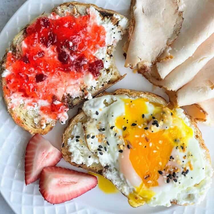 Whipped feta with pepper jelly on toast and whipped feta with an over easy egg on a bagel with berries and sliced turkey on a plate.
