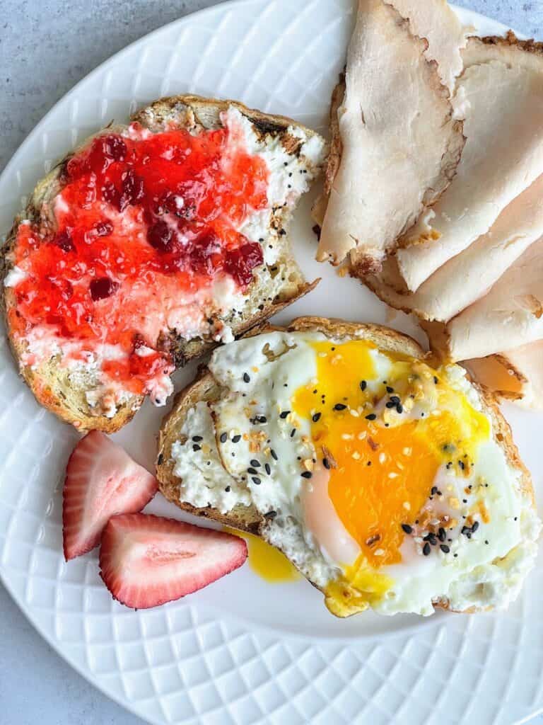 Whipped feta with pepper jelly on toast and whipped feta with an over easy egg on a bagel with berries and sliced turkey on a plate.