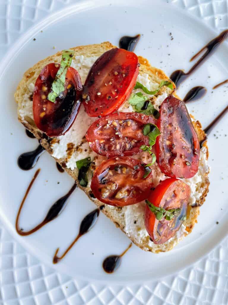 Marinated Tomatoes + Basil + Balsamic Glaze with Whipped Fet on toast on a plate.