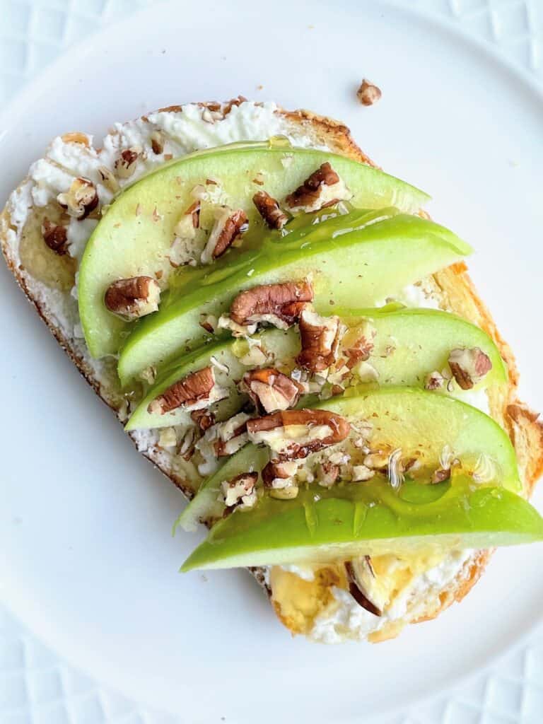Granny Smith Apple + Crushed Pecans + Honey with Whipped Feta on toast on a plate.