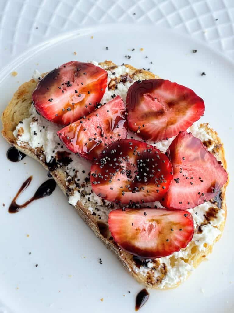 Sliced Strawberries, Balsamic Glaze, Chia Seeds, and Whipped Feta on toast on a plate.