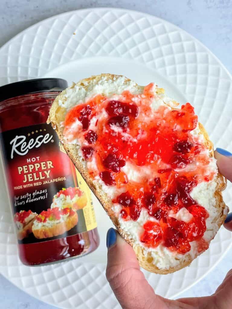 A hand holding Whipped Feta with pepper jelly on toast.