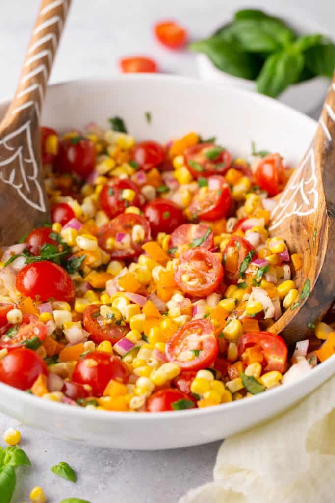 Rainbow corn salad in a large bowl with a wooden spoon.