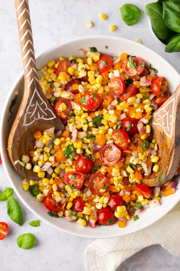 Rainbow corn salad in a large bowl with a wooden spoon.