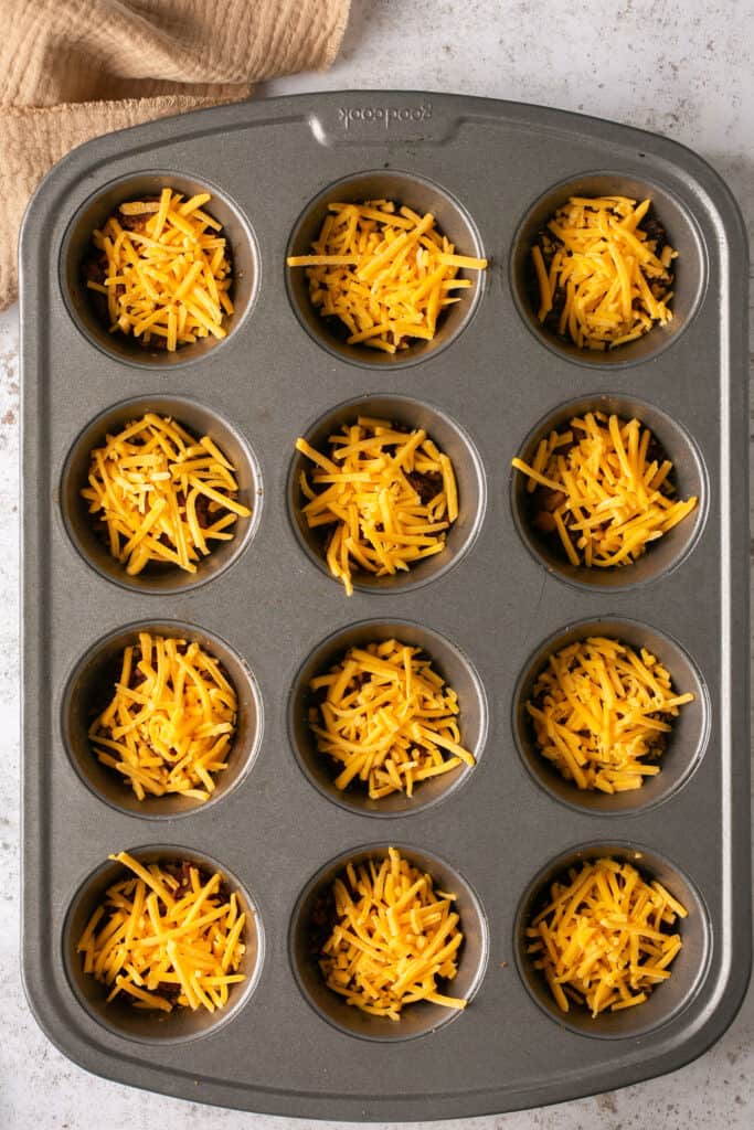 Bacon topped with shredded cheese in a muffin tin.