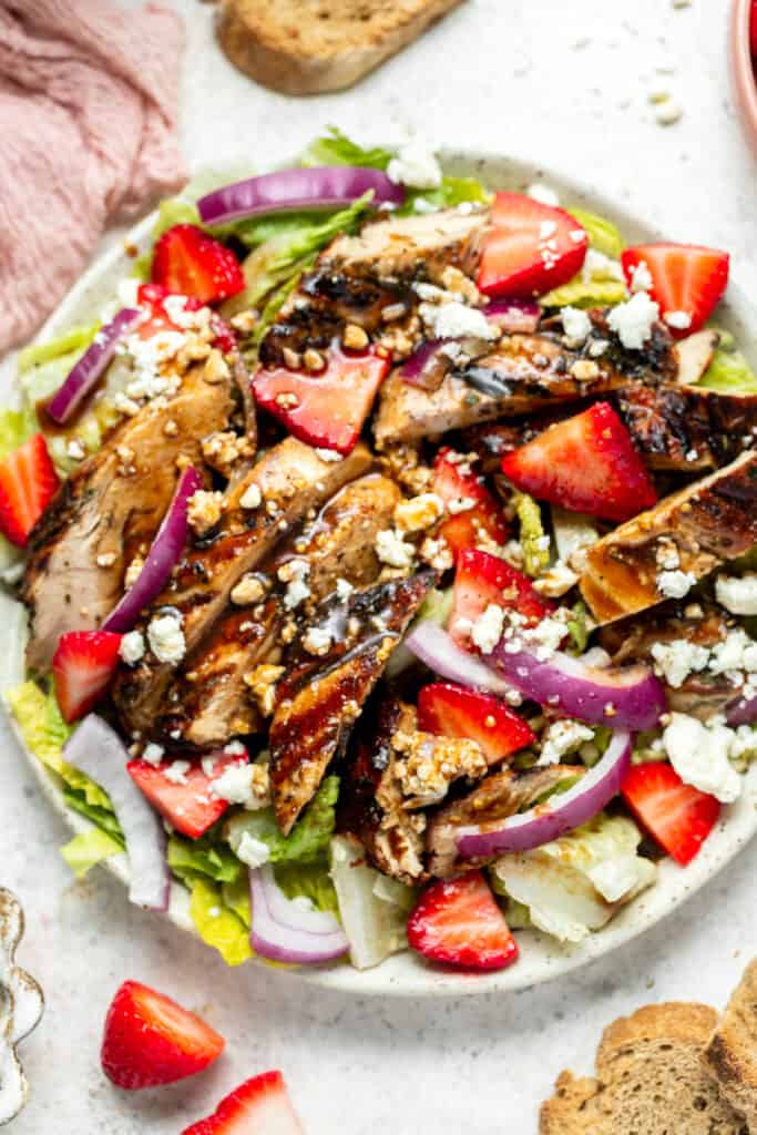 Close up of Balsamic Grilled Chicken Salad with Strawberries and Goat Cheese topped with balsamic dressing served in a bowl