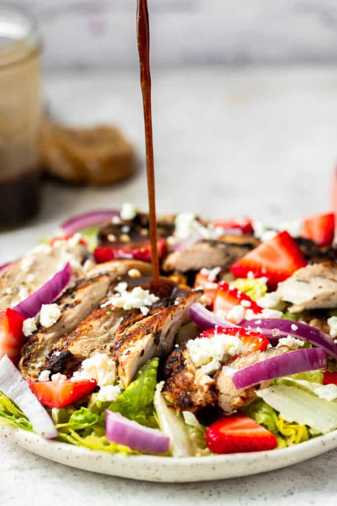 Balsamic grilled chicken salad being topped with light balsamic dressing on a plate.