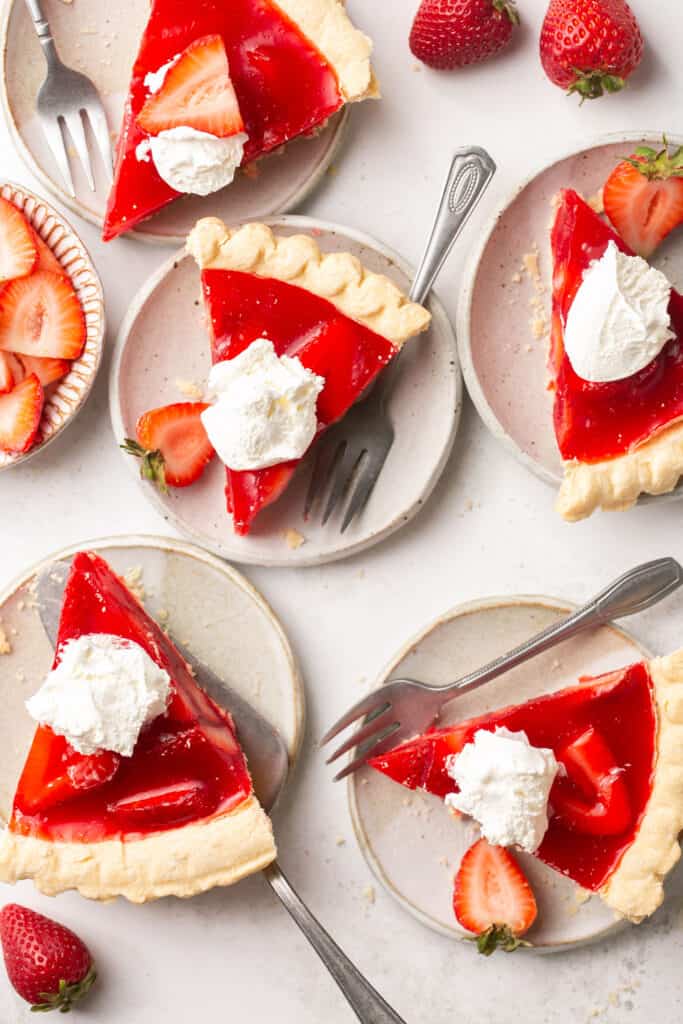 lots of slices of strawberry pie with jello topped with whipped cream on a plate. 