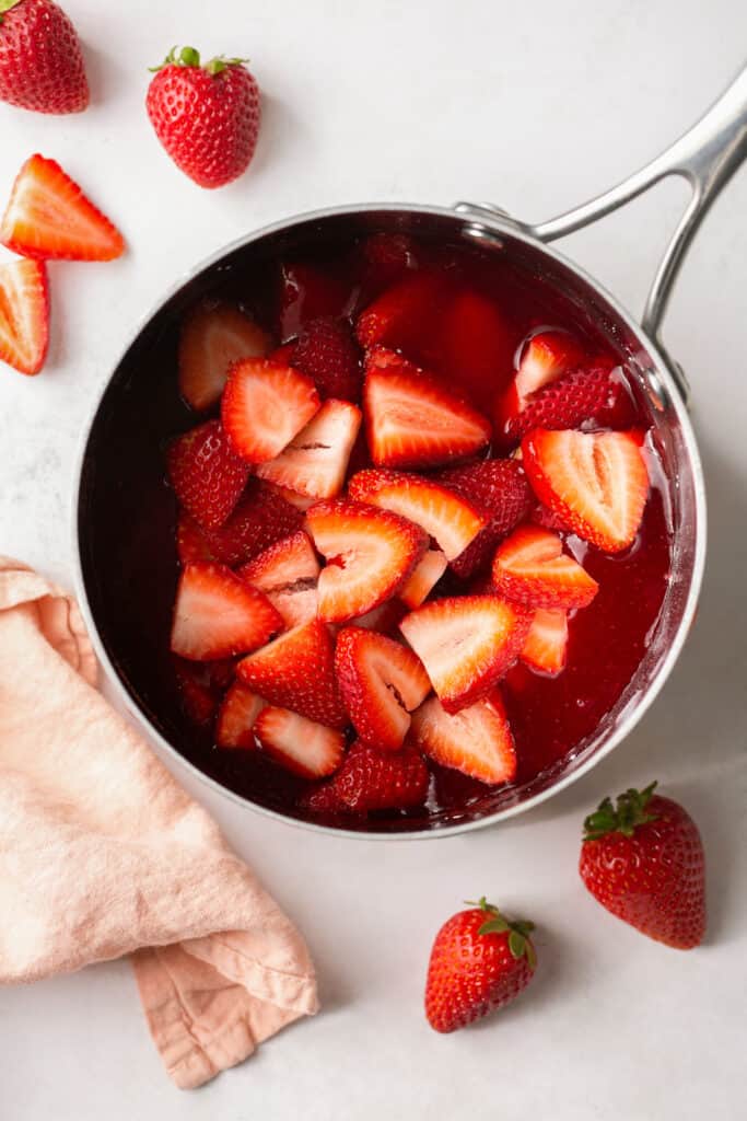 Sliced strawberries added to the mixture in the saucepan.