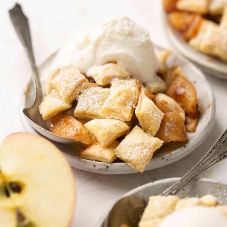 Apple puff pastry served on a small plate with a spoon and topped with vanilla ice cream.