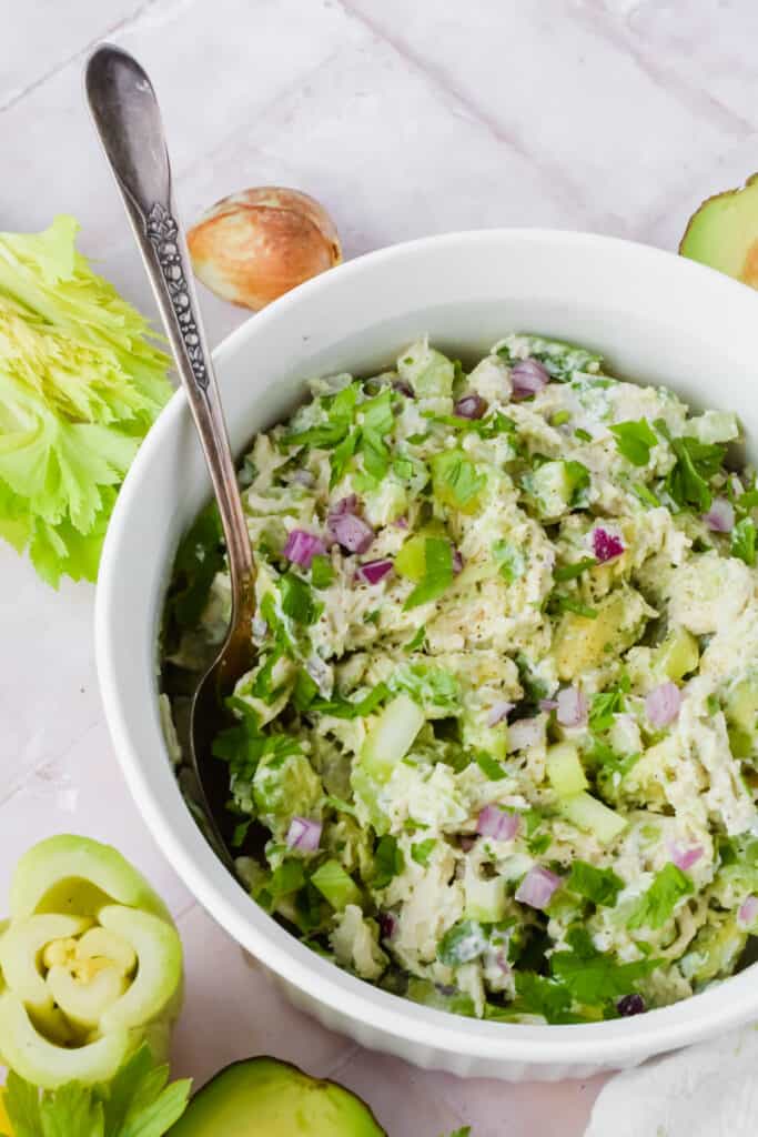 Avocado chicken salad in white bowl with serving spoon.