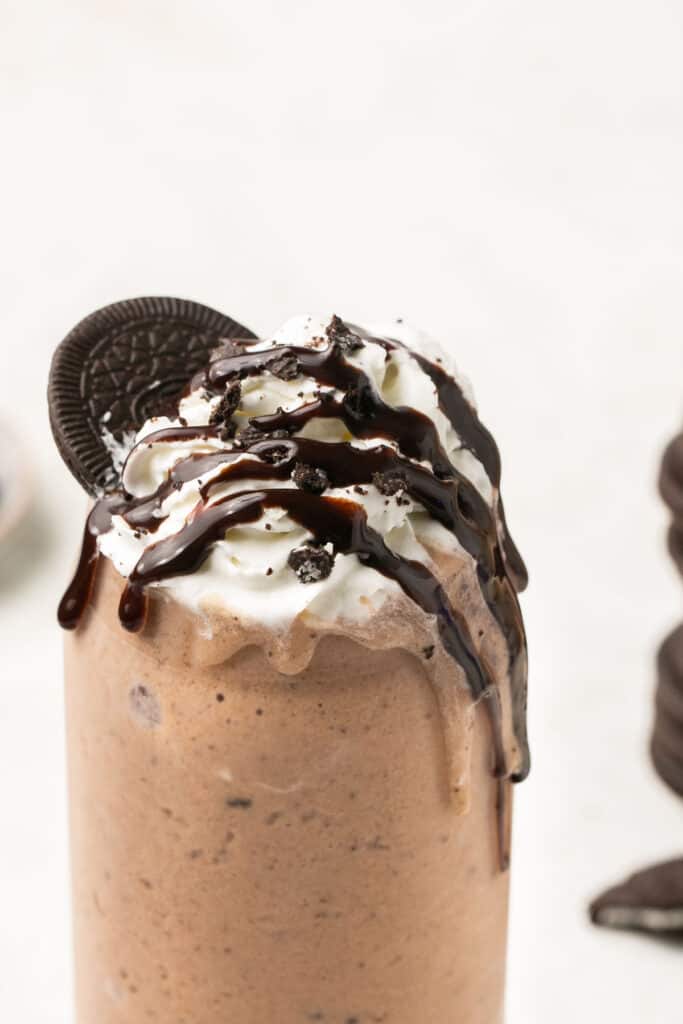 Cookies and cream protein shake in a tall glass topped with whipped cream, chocolate syrup, and Oreos.