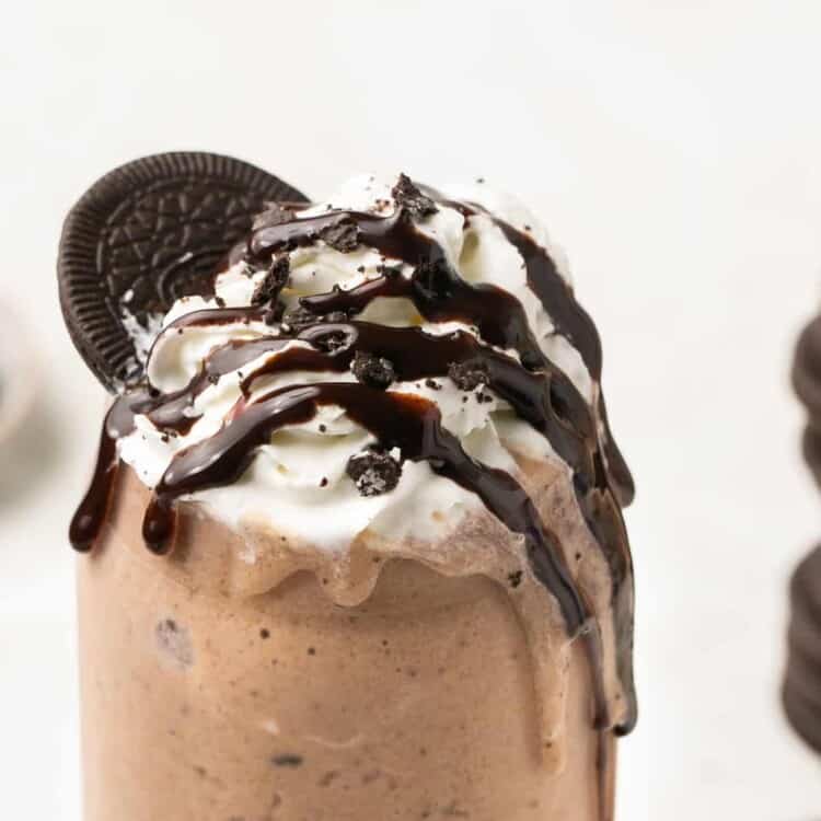 Cookies and cream protein shake in a tall glass topped with whipped cream, chocolate syrup, and Oreos.
