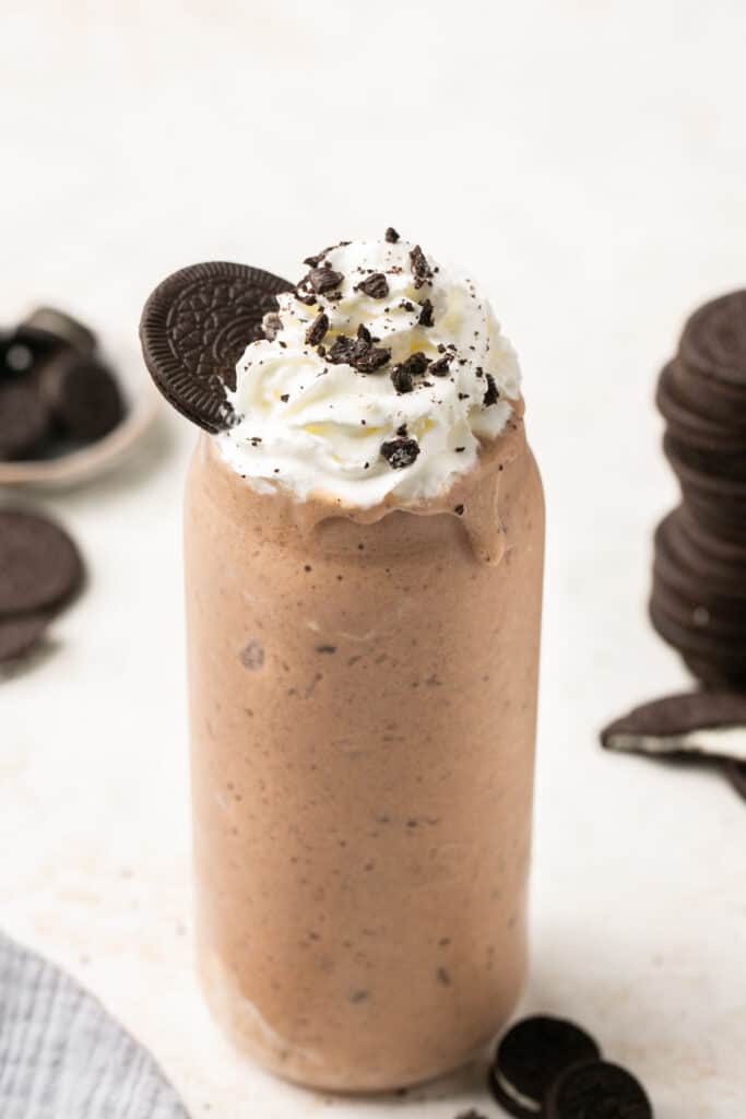 Cookies and cream protein shake in a tall glass topped with whipped cream, chocolate syrup, and Oreos.