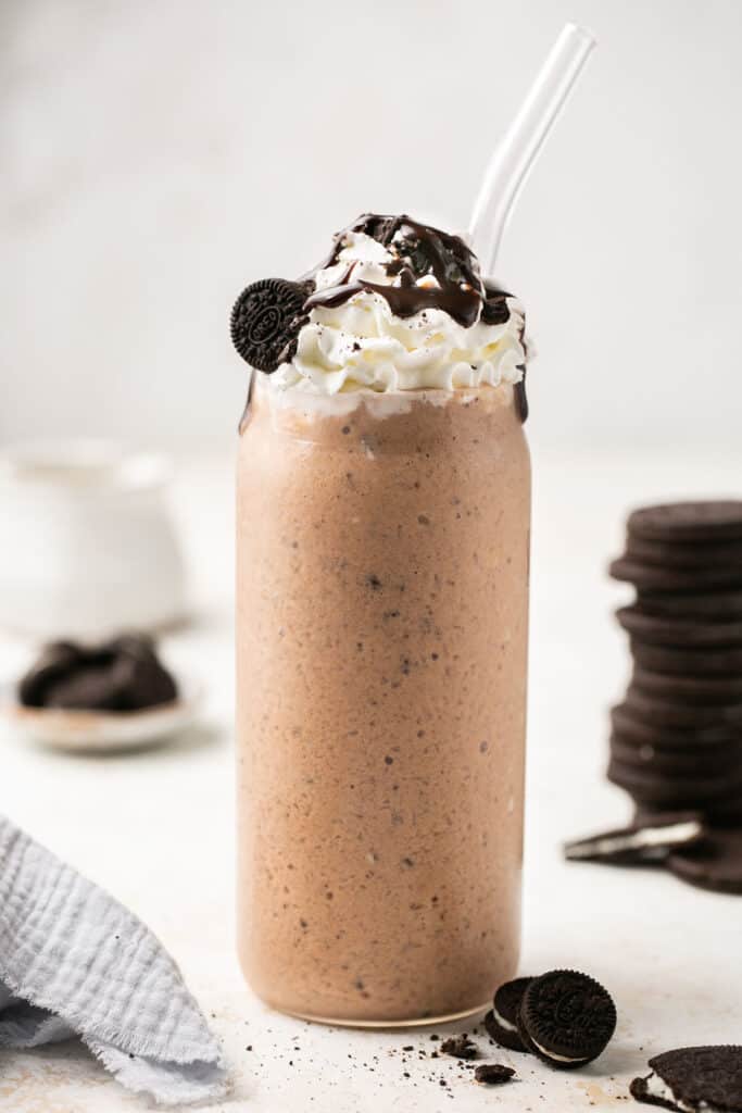 Cookies and cream protein shake in a tall glass topped with whipped cream, chocolate syrup, and Oreos.