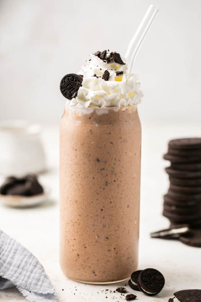 Cookies and cream protein shake in a tall glass topped with whipped cream, chocolate syrup, and Oreos.