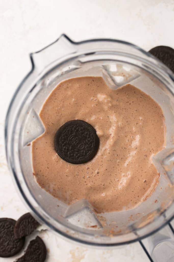 An oreo in a food processor bowl along with the combined ingredients for cookies and cream protein shake.