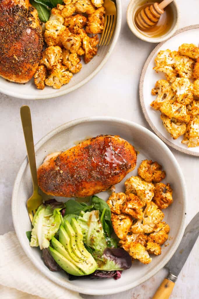 Honey garlic baked chicken and cauliflower served on a plate with greens and avocado