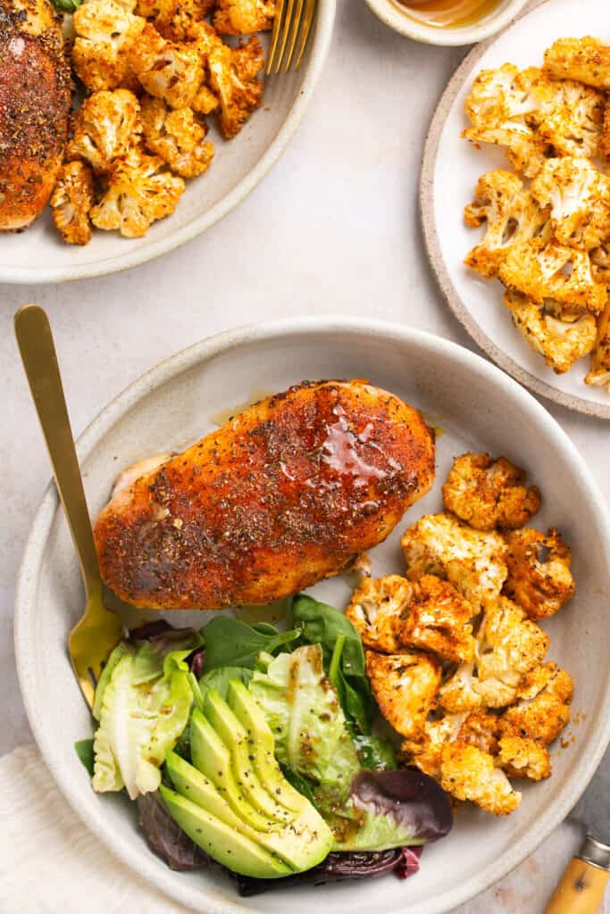 Honey garlic baked chicken and cauliflower recipe served on a plate with a fork alongside greens and avocado