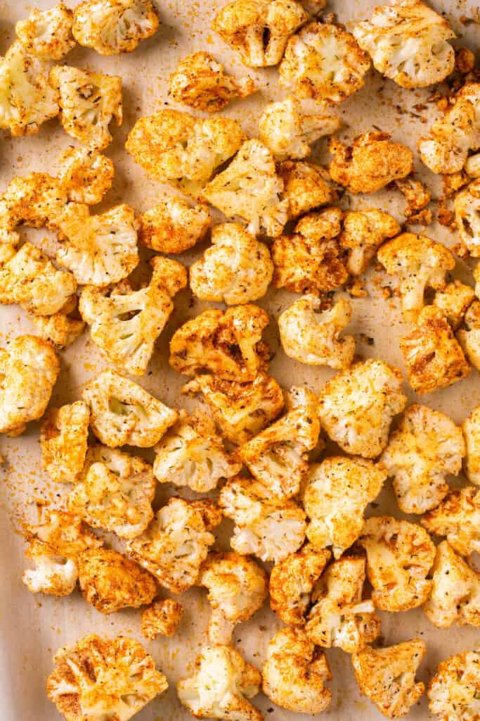 Cut up cauliflower sprinkled with seasonings on a baking sheet with parchment paper.