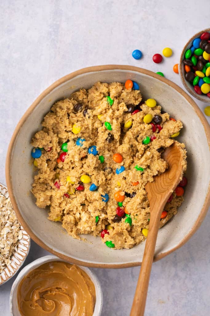 M&Ms mixed together with the rest of the cookie dough ingredients with a wooden spoon.