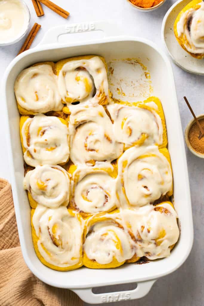 Healthy pumpkin cinnamon rolls topped with cream cheese icing in a baking dish