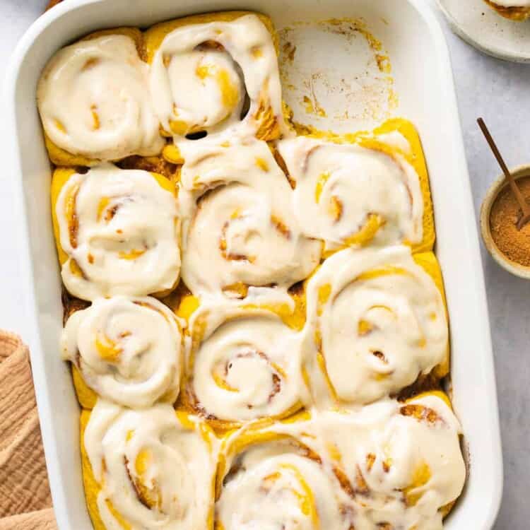 Pumpkin Cinnamon rolls topped with icing in a baking dish.