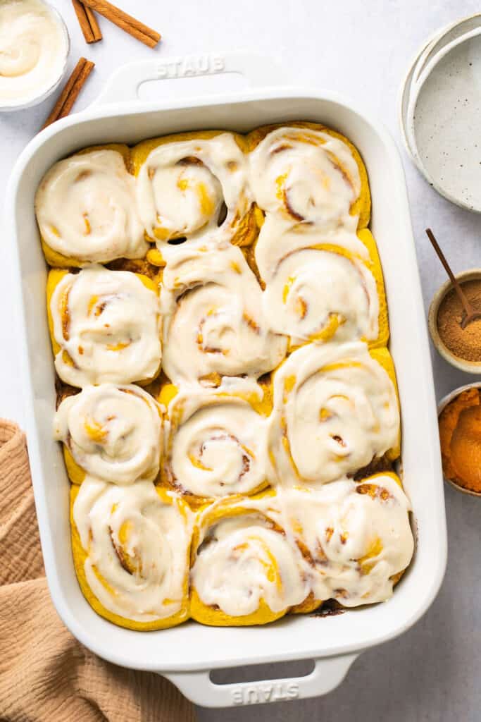 Healthy pumpkin cinnamon rolls topped with cream cheese icing in a baking dish after being baked