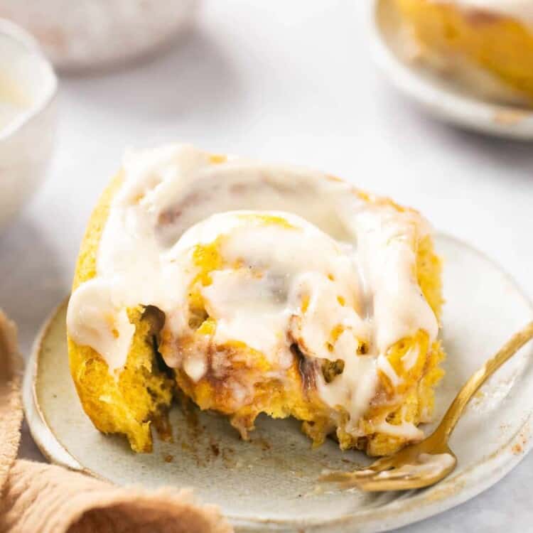 Healthy pumpkin cinnamon roll with cream cheese icing served on a small plate with a fork with a bite taken out of it.