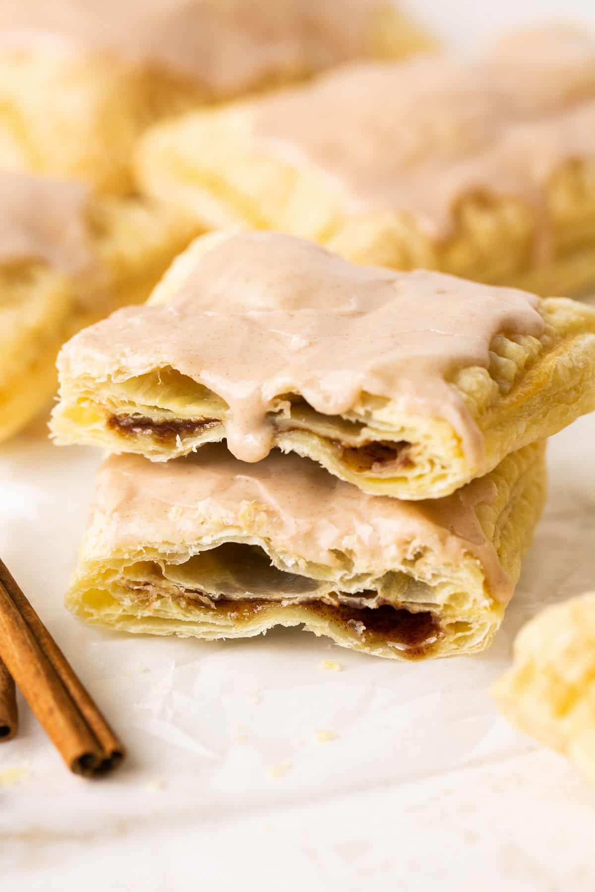 Air fryer pop tart broken in half with a crisp, flaky crust and brown sugar filling, topped with frosting and garnished with cinnamon sticks.