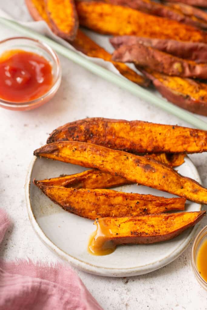 Crispy air fryer sweet potato wedges on a small plate with dipping sauce on the side