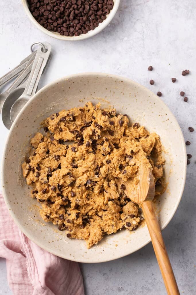 Chocolate chip cookie dough in a bowl with a wooden spoon before being formed into bites