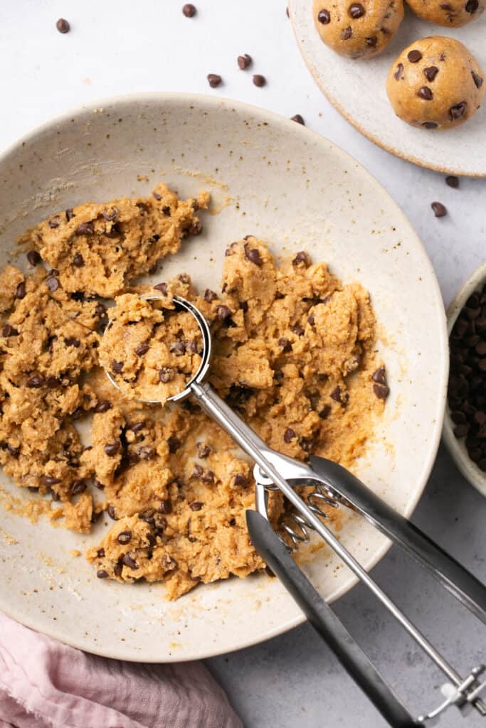 Cookie dough protein bites mixture in a bowl with a cookie scoop.