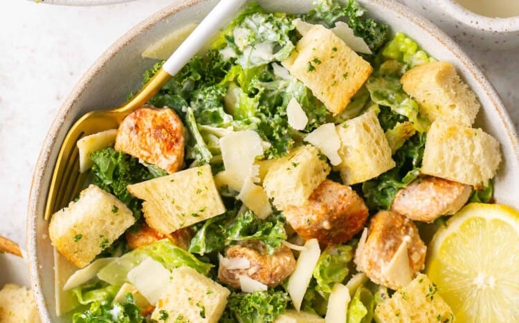 Healthy chicken caesar salad topped with croutons in a bowl with a fork.