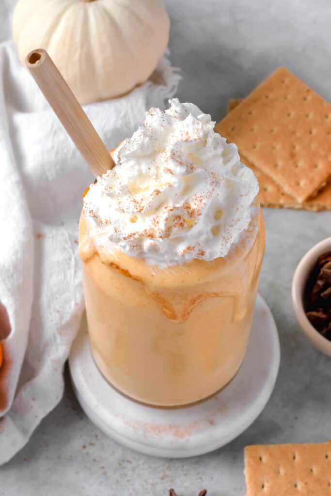 Pumpkin protein shake recipe served in a jar with a straw topped with whipped cream.