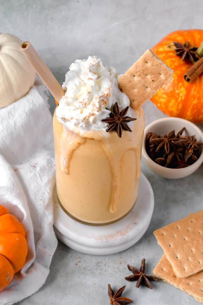 Pumpkin protein shake served in a jar with a straw topped with whipped cream and graham crackers.