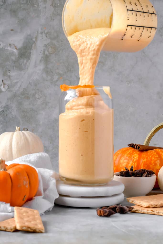 Pumpkin protein shake being prourd from a blender container into a tall glass.